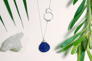 Silver lapis necklace laying on a flat background the necklace features three hammered circles two of them interlinked cutting into the chain