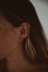 Woman wearing ruins studs in second piercing hole studs are a geometric V shape