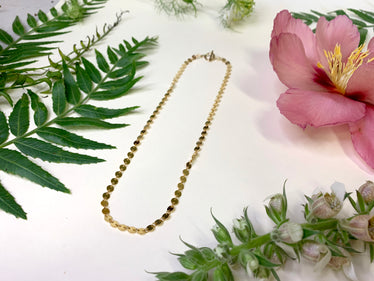 Sequin chain necklace on white background with decorative flowers