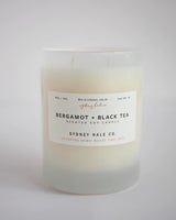 Cream coloured candle in frosted white glass jar with a white label and black text 