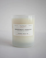 Cream coloured candle in frosted white glass jar with white label in neutral background￼