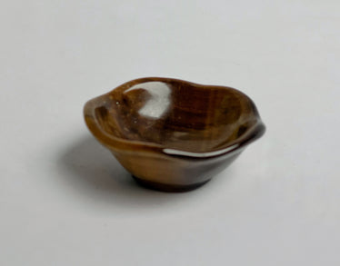 small bowl carved out of tigers eye stone sitting on neutral background