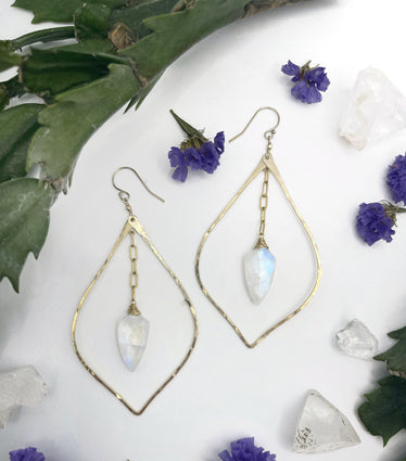 hammered petal moonstone drop earrings on white background earrings consist of a hammered pointed teardrop shape resembling a petal with a spade shaped moonstone hanging in the middle off of a small length of chain￼