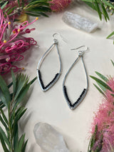 Two silver earrings on a white background with crystal and flowers. The earrings are white pointed teardrop shapes resembling a flower petal. The shape is a hammered silver bar with tiny black beads lined up and wrapped with wire into the bottom middle of the shape. 