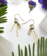 two earrings laying flat on white background each earring features two gold sticks hanging next to a small wire wrapped citrine stone￼