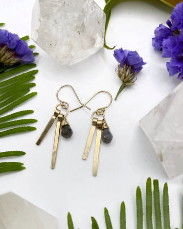 hammered Fringe Herkimer diamond earrings laying flat on white background featuring two metal sticks hanging next to a wire wrapped teardrop labradorite stone￼