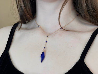 
Woman wearing diamond drop necklace chain lays across the top of collarbones featuring a drop lariat of a blue Lapis diamond with beads cut into the chain￼