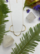 triple arc necklace laying flat on white background with leaves￼