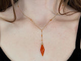 Woman wearing diamond drop necklace in gold. the chain lays over the top of collarbones featuring a drop lariat of orange carnelian stone with orange carnelian cut in beads throughout the train￼