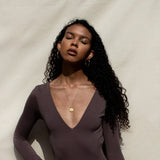 Woman wearing gold Roma necklace in direct sunlight light bouncing off of pendant
