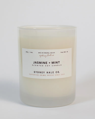 Cream coloured candle in frosted glass jar with white label in neutral background